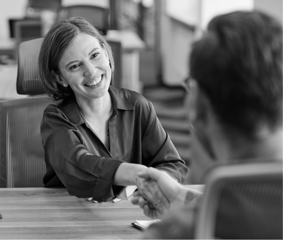 Image of two people shaking and hiring a new team member. A temp worker is seen smiling while at an interview accepting a job.